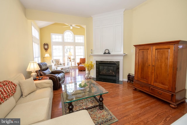 living area featuring vaulted ceiling, a large fireplace, ceiling fan, and wood finished floors