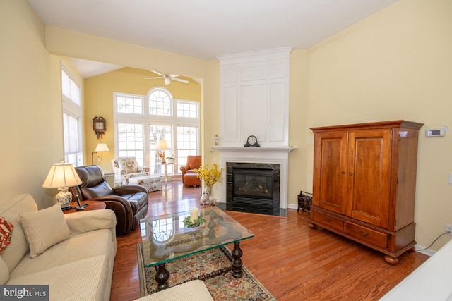 living room with a high end fireplace, a ceiling fan, lofted ceiling, and wood finished floors