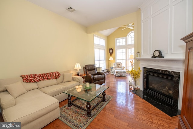 living room with visible vents, a ceiling fan, a fireplace, light wood finished floors, and vaulted ceiling