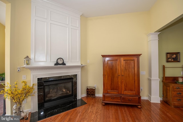 interior space featuring wood finished floors, decorative columns, a fireplace, and baseboards