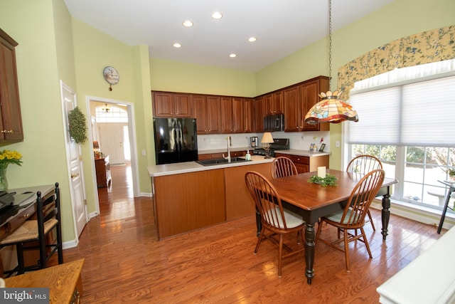 kitchen featuring black appliances, an island with sink, a sink, wood finished floors, and a healthy amount of sunlight