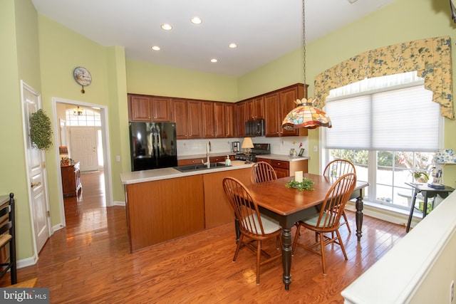 kitchen featuring black appliances, an island with sink, a sink, tasteful backsplash, and wood finished floors