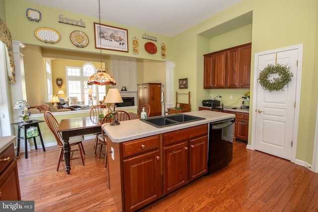 kitchen featuring decorative columns, a sink, light countertops, black dishwasher, and light wood-type flooring