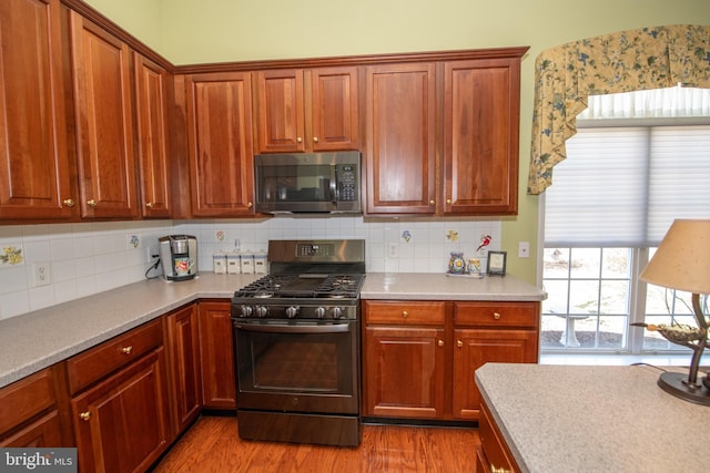 kitchen with wood finished floors, decorative backsplash, light countertops, black range with gas cooktop, and stainless steel microwave