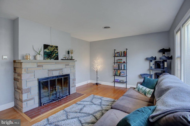 living area featuring visible vents, a stone fireplace, baseboards, and wood finished floors