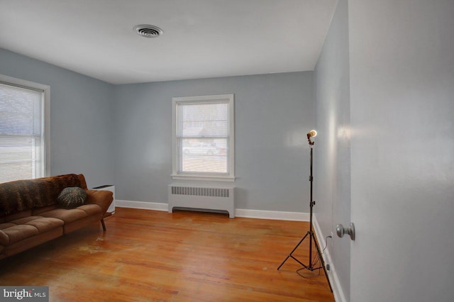 sitting room featuring light wood-type flooring, visible vents, baseboards, and radiator heating unit