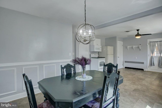 dining room with a wainscoted wall, ceiling fan with notable chandelier, radiator, and a decorative wall