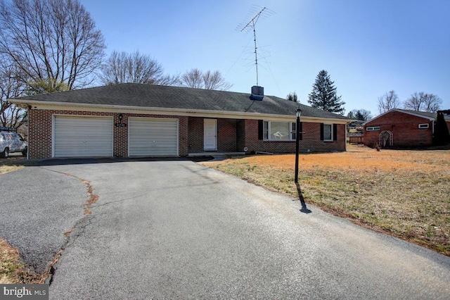 ranch-style house featuring driveway, an attached garage, a front yard, brick siding, and a chimney