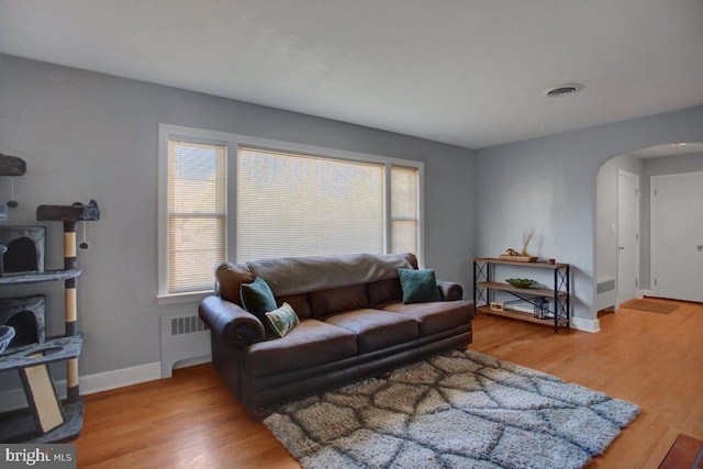 living room featuring arched walkways, visible vents, radiator heating unit, and wood finished floors