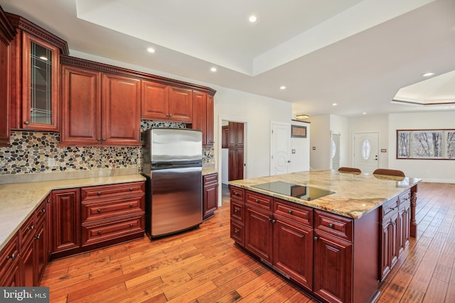 kitchen featuring light wood finished floors, freestanding refrigerator, a raised ceiling, black electric stovetop, and reddish brown cabinets