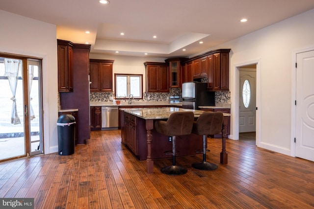 kitchen with dark wood-type flooring, a tray ceiling, backsplash, and stainless steel appliances