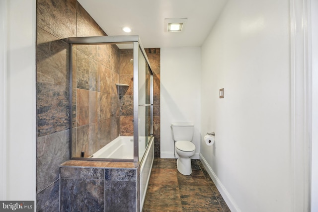 bathroom featuring combined bath / shower with glass door, toilet, stone finish flooring, and baseboards