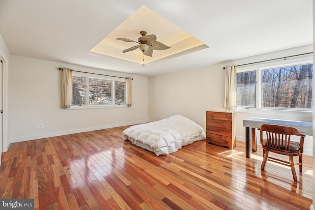 bedroom with a tray ceiling, multiple windows, light wood-style floors, and baseboards