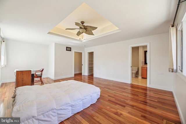 bedroom with light wood-type flooring, a raised ceiling, and baseboards