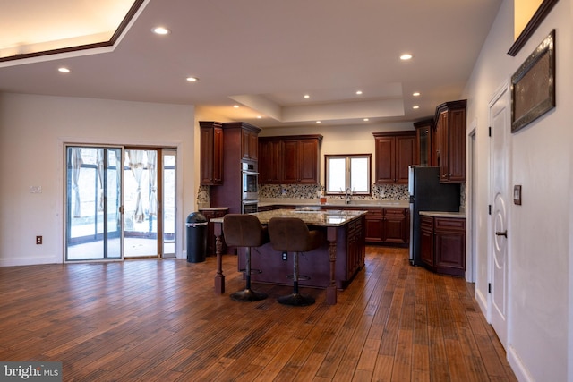 kitchen with backsplash, a center island, a tray ceiling, freestanding refrigerator, and dark wood-style flooring