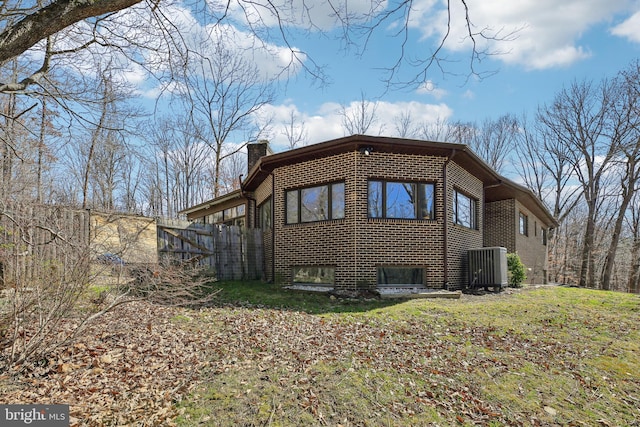 view of property exterior featuring brick siding, central AC unit, a chimney, and fence