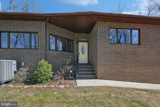 view of exterior entry with cooling unit and brick siding