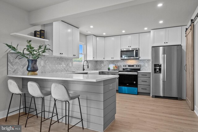 kitchen with a barn door, light wood-style flooring, a peninsula, stainless steel appliances, and open shelves