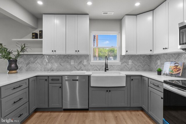 kitchen featuring open shelves, light wood-style flooring, a sink, gray cabinetry, and stainless steel appliances