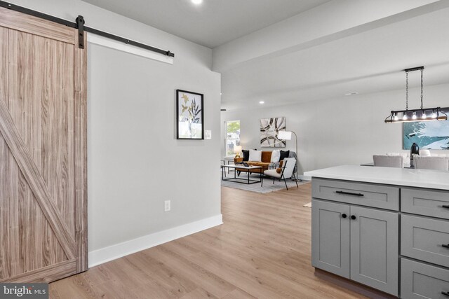 kitchen with light wood finished floors, gray cabinetry, a barn door, light countertops, and baseboards