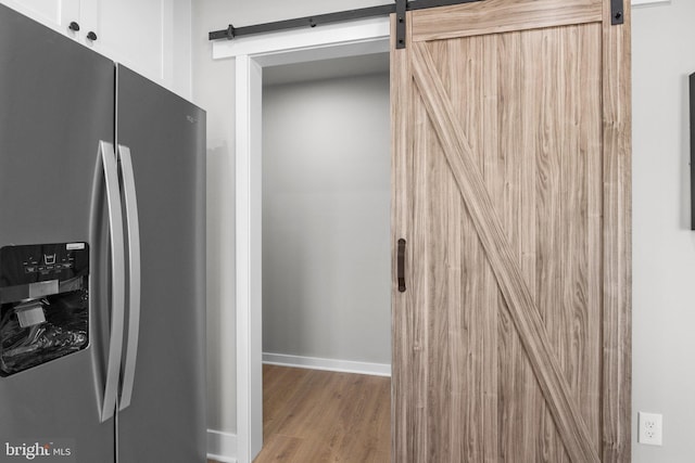 kitchen featuring stainless steel refrigerator with ice dispenser, wood finished floors, white cabinetry, a barn door, and baseboards