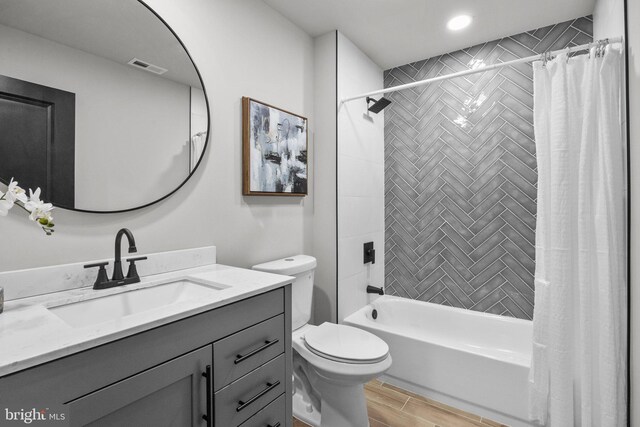 bathroom with visible vents, wood finish floors, toilet, shower / bath combination with curtain, and vanity