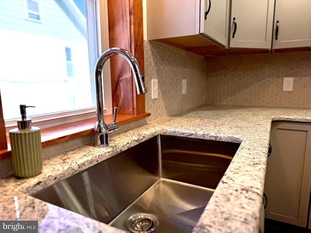 details featuring light stone counters, tasteful backsplash, and a sink