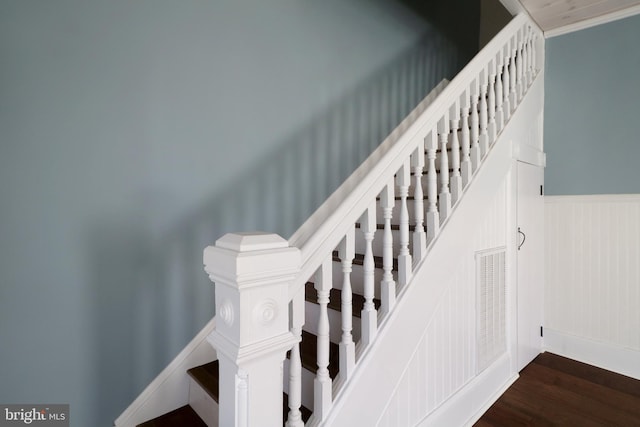 stairs featuring wood finished floors and wainscoting