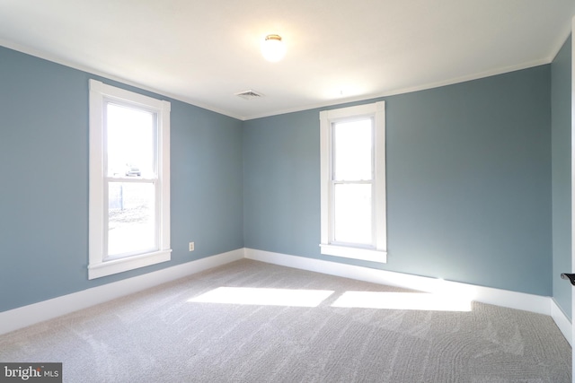 carpeted empty room with baseboards, a healthy amount of sunlight, visible vents, and ornamental molding