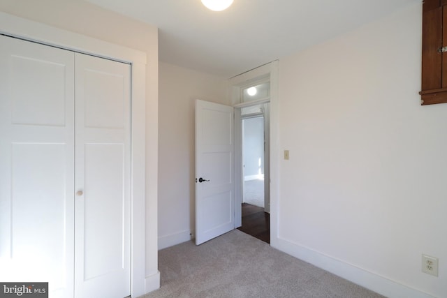 unfurnished bedroom featuring a closet, light colored carpet, and baseboards