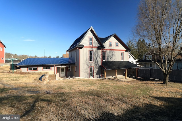 rear view of property featuring a yard, fence, and metal roof