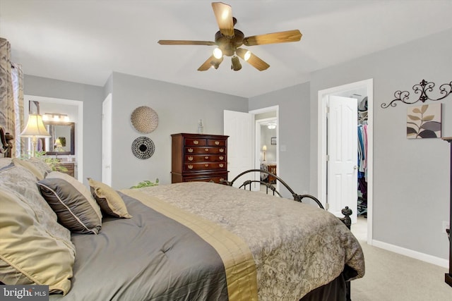 bedroom with a spacious closet, baseboards, light colored carpet, ensuite bath, and a ceiling fan