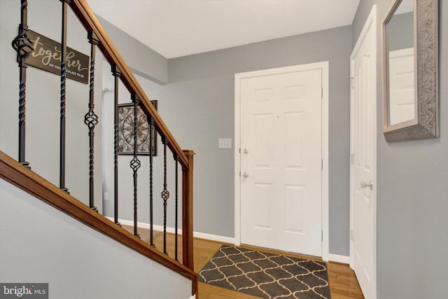 foyer entrance with stairs, wood finished floors, and baseboards