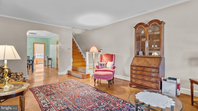 living area with stairway, arched walkways, baseboards, and ornamental molding