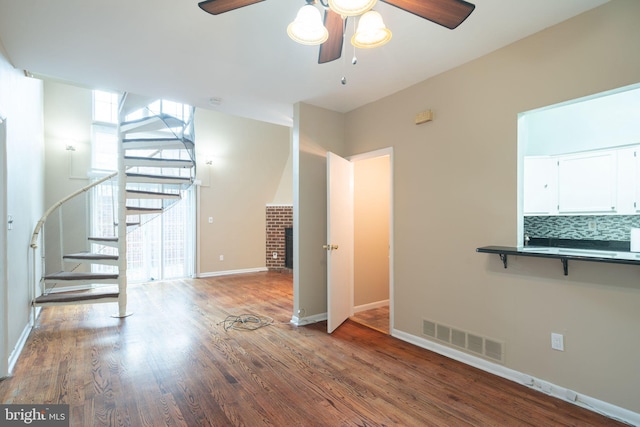 unfurnished living room featuring visible vents, wood finished floors, baseboards, a brick fireplace, and stairs