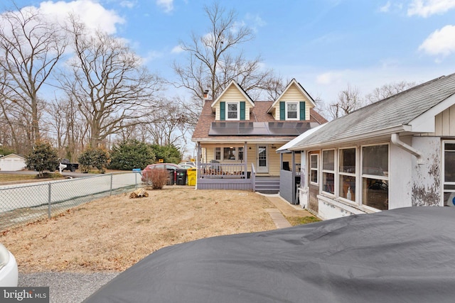 view of front facade featuring roof mounted solar panels, a porch, fence, a shingled roof, and a chimney