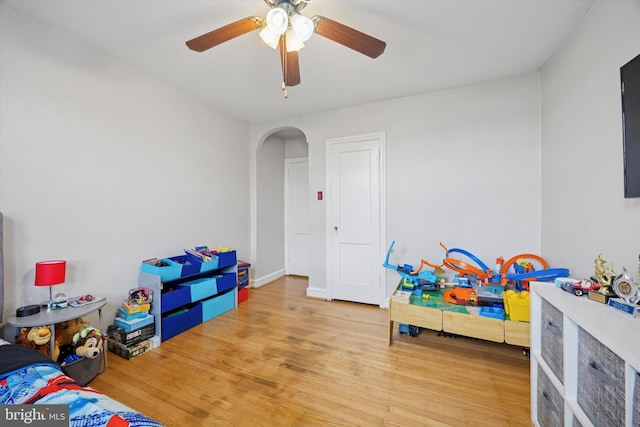 rec room with baseboards, arched walkways, wood finished floors, and a ceiling fan