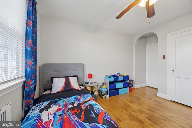 bedroom with arched walkways, baseboards, ceiling fan, and wood finished floors