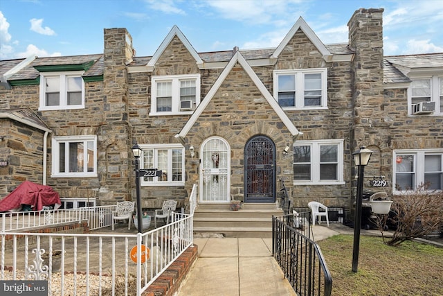 view of front of property featuring cooling unit, stone siding, and fence