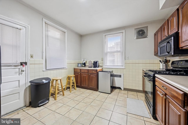 kitchen featuring black appliances, radiator, tile walls, wainscoting, and light tile patterned floors