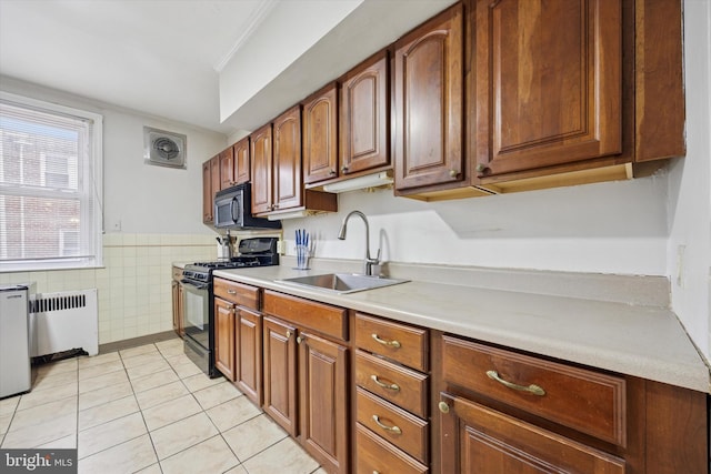 kitchen with black appliances, a sink, radiator, tile walls, and light tile patterned floors