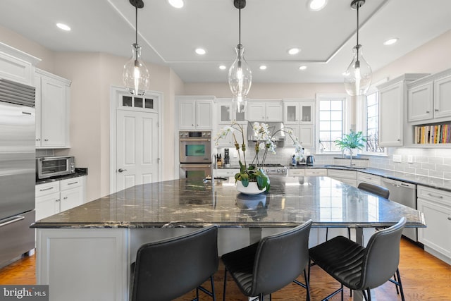 kitchen featuring light wood finished floors, backsplash, a center island with sink, appliances with stainless steel finishes, and white cabinets