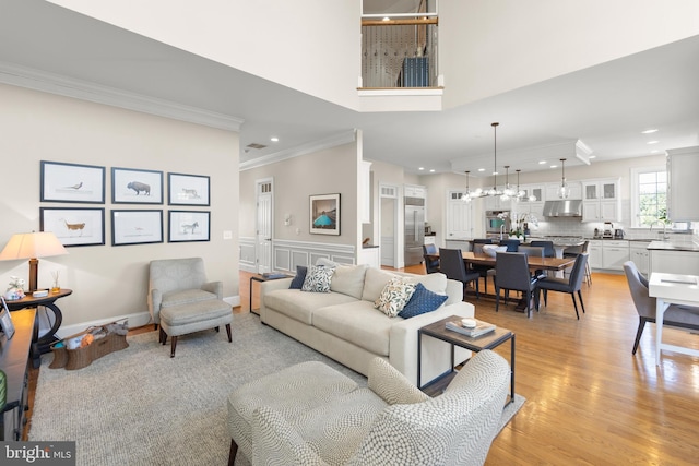 living area featuring recessed lighting, light wood-style flooring, crown molding, and a high ceiling