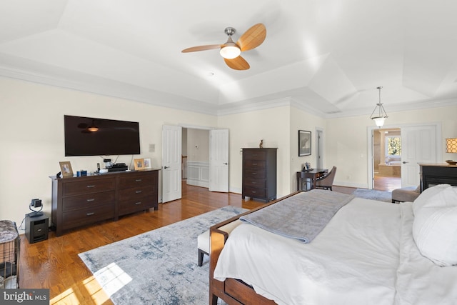 bedroom with a ceiling fan, a raised ceiling, wood finished floors, and ornamental molding