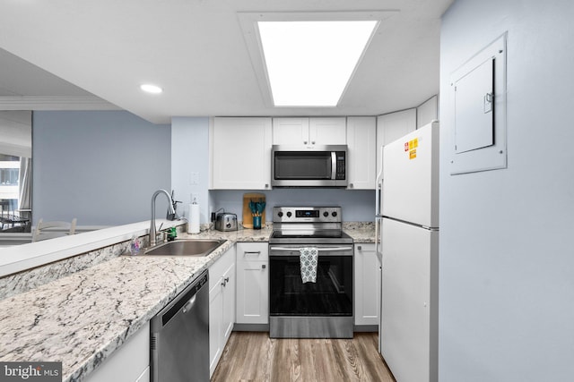 kitchen featuring light wood finished floors, light stone countertops, appliances with stainless steel finishes, white cabinets, and a sink