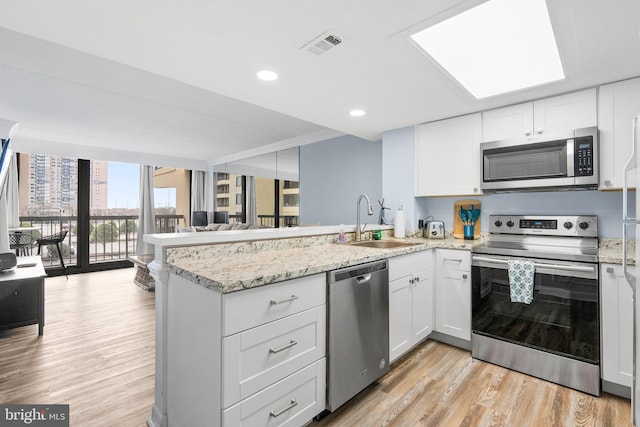 kitchen with light wood-type flooring, visible vents, a sink, stainless steel appliances, and a peninsula