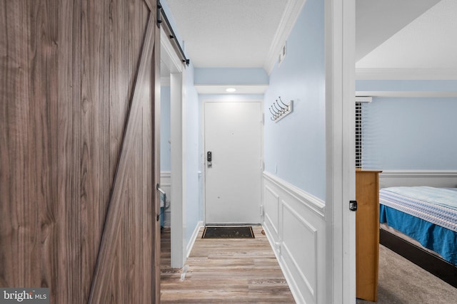 hall featuring light wood finished floors, crown molding, wainscoting, a barn door, and a decorative wall