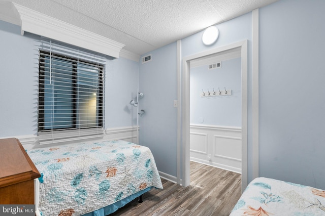 bedroom featuring visible vents, a textured ceiling, wood finished floors, and a decorative wall