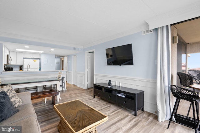 living area featuring light wood-type flooring, a wainscoted wall, visible vents, and ornamental molding
