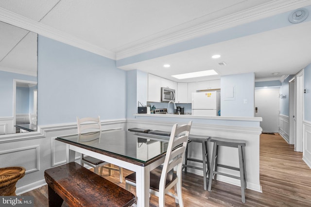 dining room featuring a wainscoted wall, wood finished floors, a skylight, crown molding, and a decorative wall